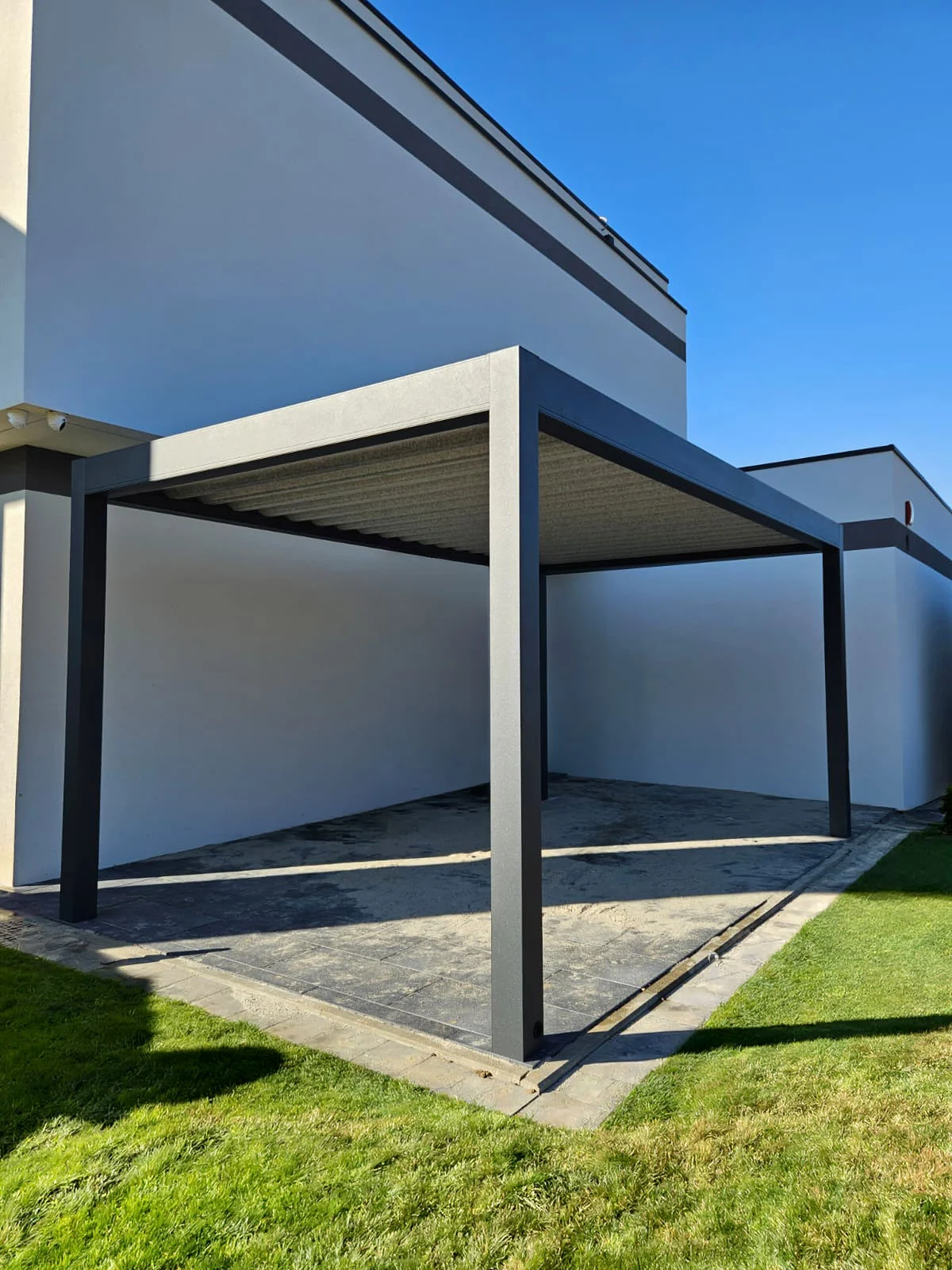 Wolnostojący carport z ciemną konstrukcją przy ogrodzeniu