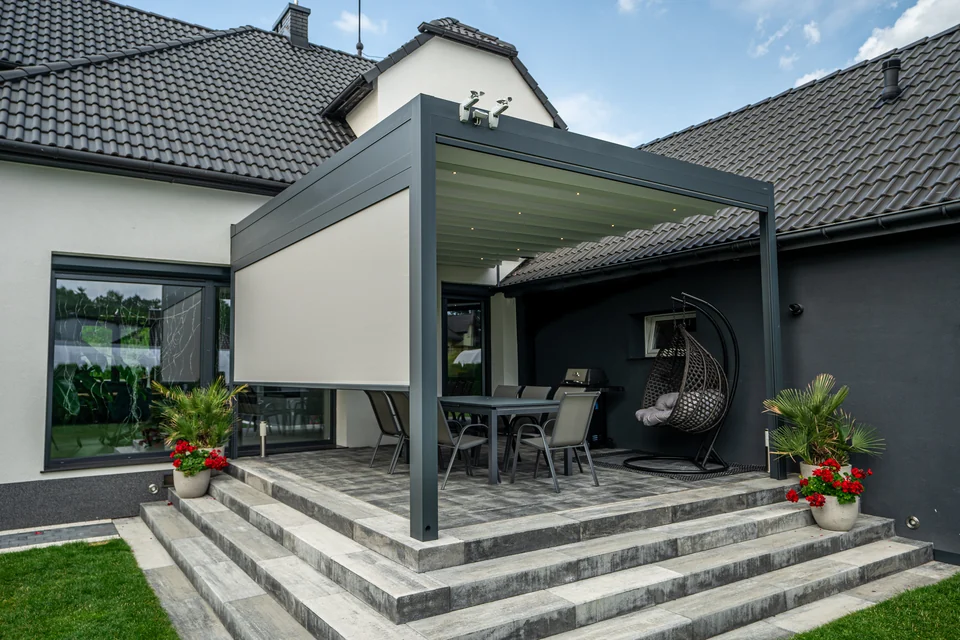 Grafitowa pergola z boczną osłoną nad tarasem ze schodami i meblami