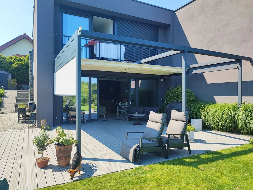 Grafitowa pergola przy piętrowym domu z fotelami na tarasie