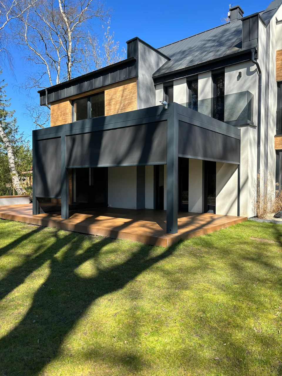 Pergola na drewnianym tarasie przy elewacji z drewna i jasnego tynku