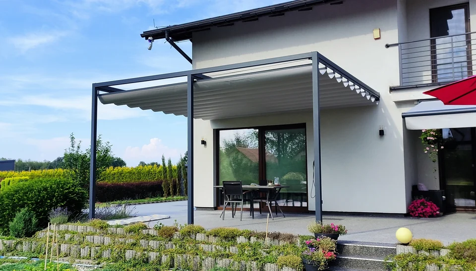 Pergola z jasnym dachem materiałowym nad tarasem ze stołem i krzesłami