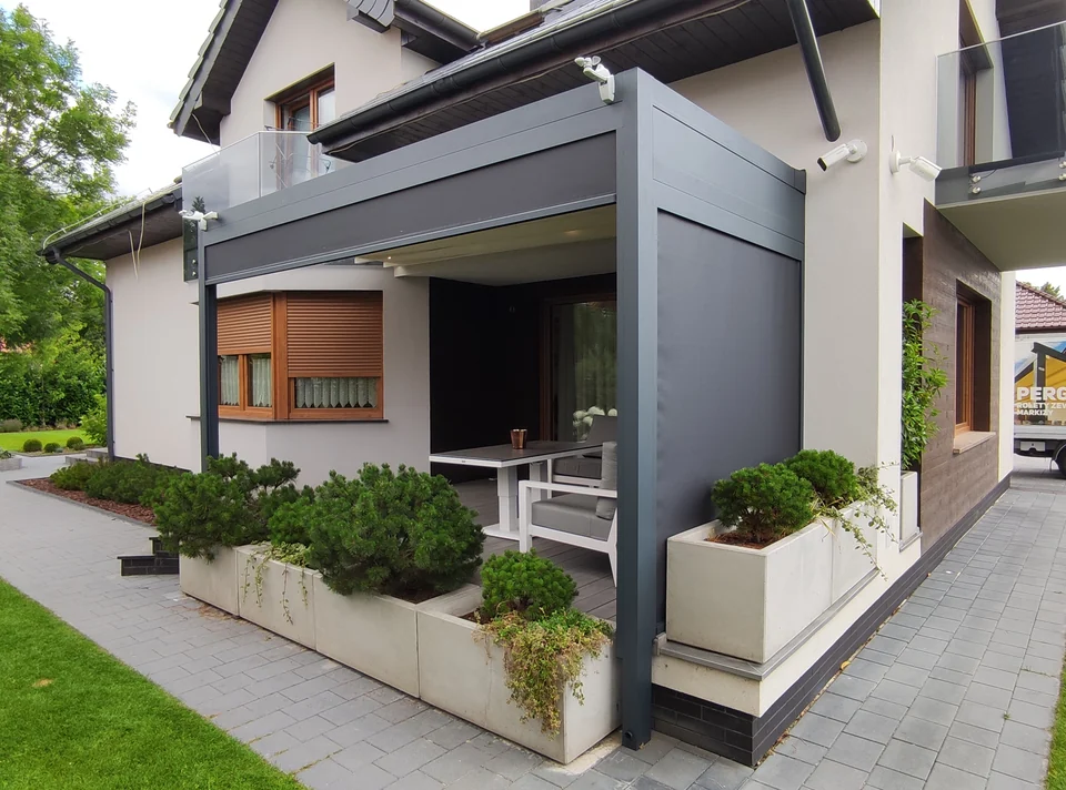 Pergola z jasnym dachem i boczną osłoną nad tarasem z dużymi donicami