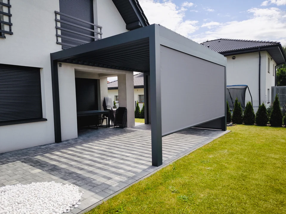 Pergola z jasną osłoną boczną nad tarasem z szarej kostki